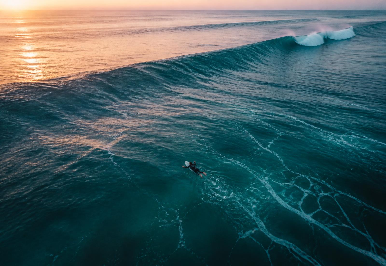 Aerial view of a surfer paddling into a clean dawn swell